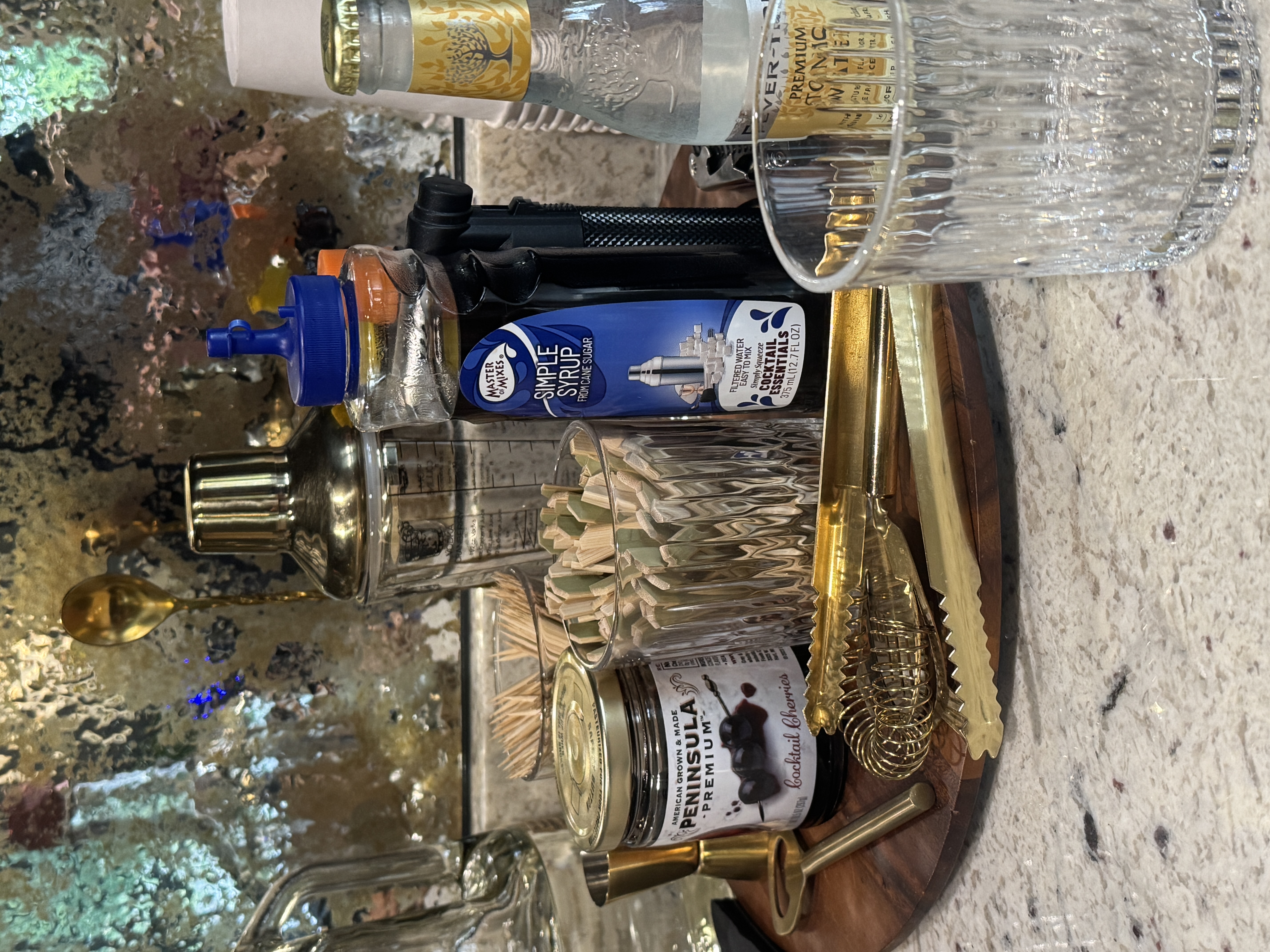 The bar setup at Chartwell: brass shaker, tongs and strainer, cocktail cherries, picks and tonic on a wood tray against an antique mirror