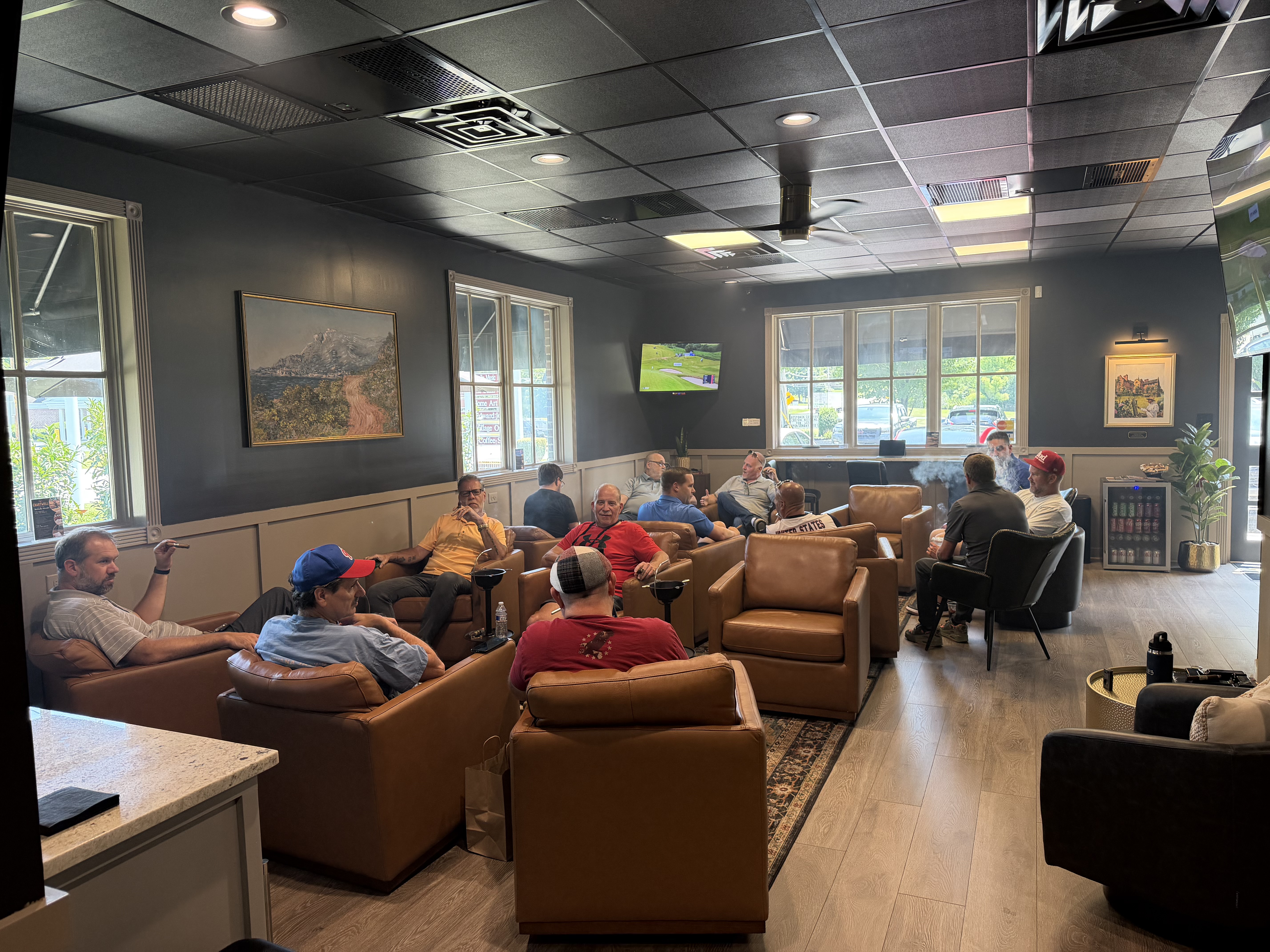 A full lounge on a Saturday afternoon: members in tan leather club chairs, cigars lit, golf on the television