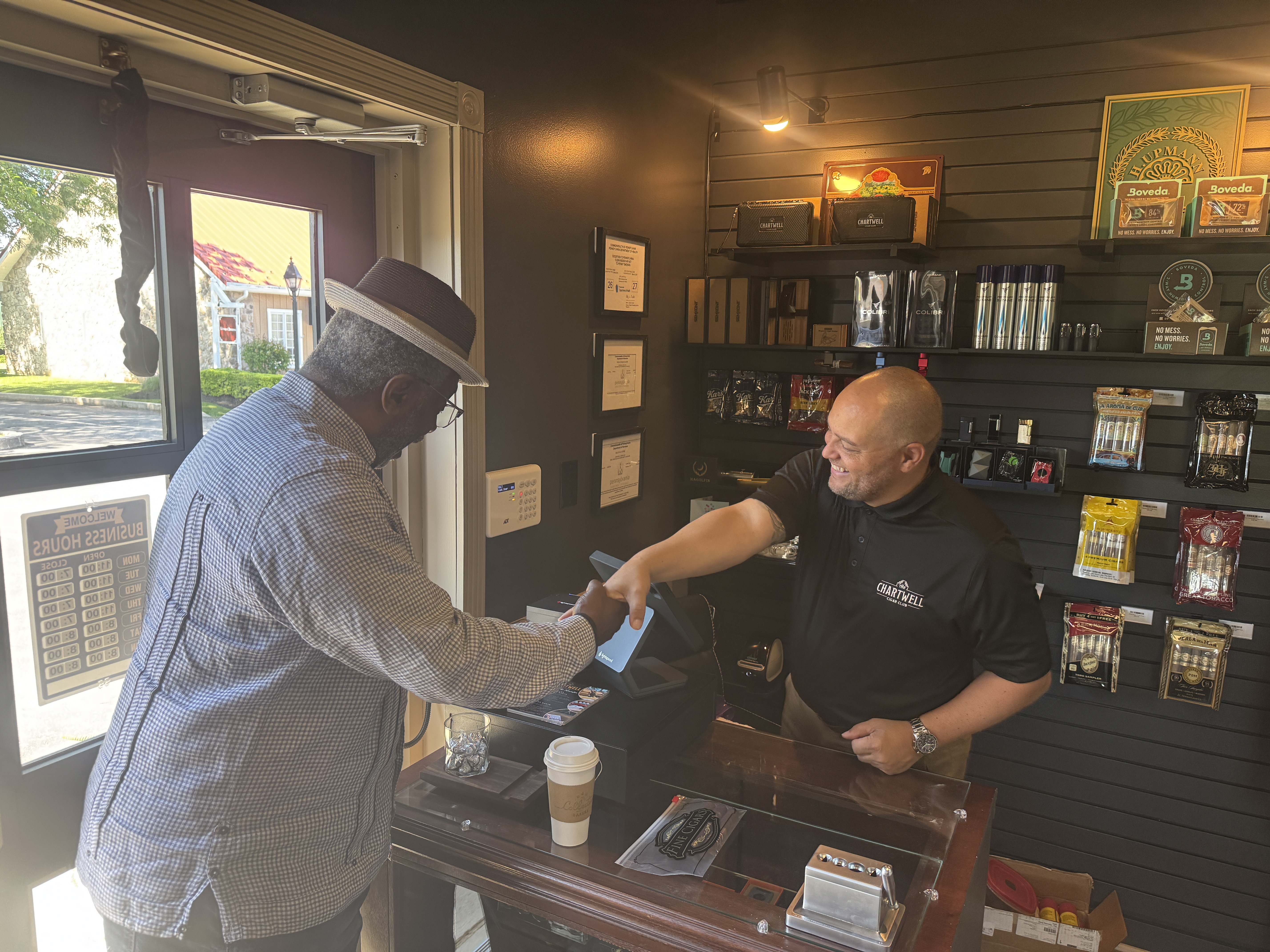 Will, in a Chartwell shirt, shaking hands with a guest in a straw hat across the front counter